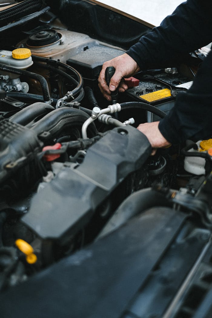Close-up of a mechanics hands working on a car engine in an indoor workshop setting.