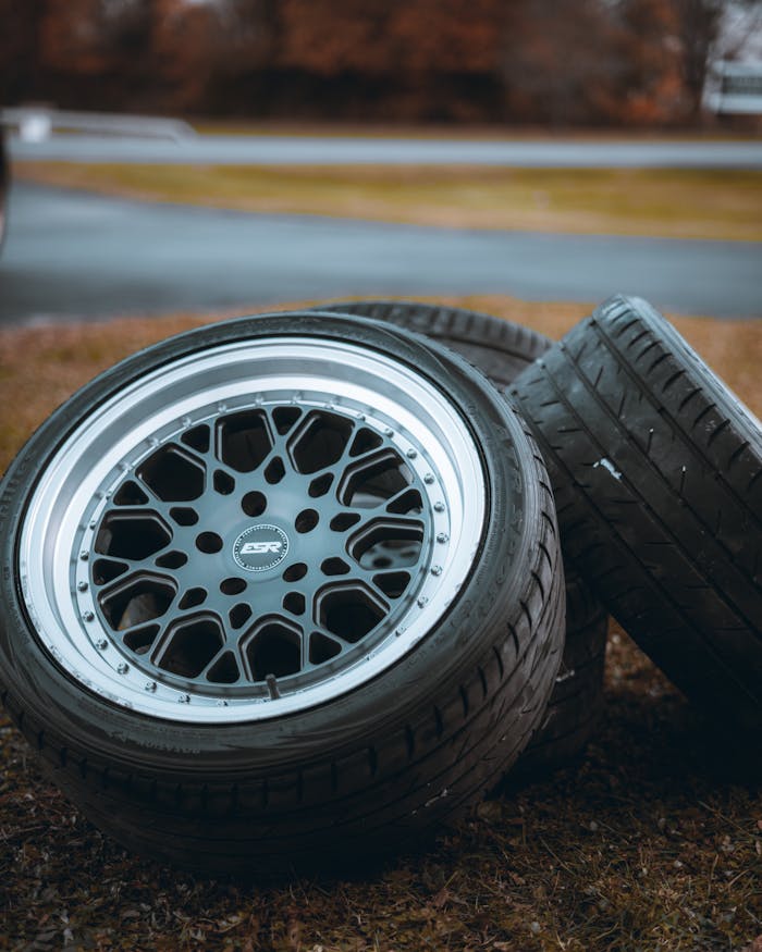Stack of glossy chrome wheels and tires on grass with blurred background, showcasing design and texture.